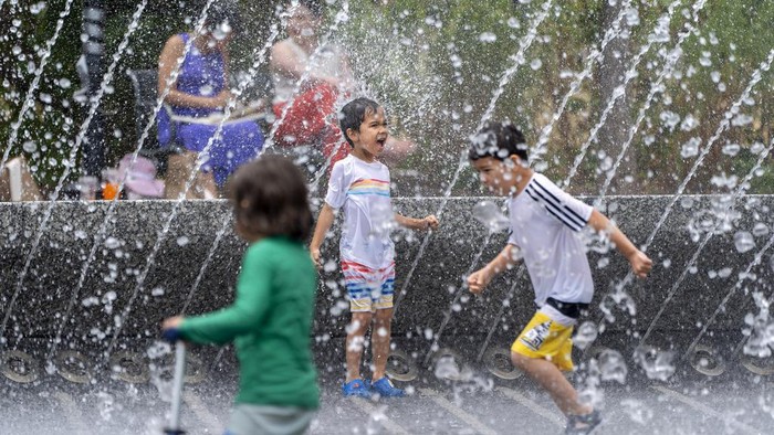 Andrea Di Miele, right, from Hoboken, N.J., puts water on his daughter, Sofia Di Miele, 10, with the Lincoln Memorial behind, near the World War II Memorial, Friday, June 21, 2024, in Washington. Temperatures are forecast to reach 100 degrees on Saturday. (AP Photo/Alex Brandon)
