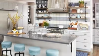 Meja dapur yang ramping dan rak terbuka di dapur ini mencerminkan gaya modern, sementara hood cooker dari kayu dan talenan serta peralatan dapur antik menciptakan tampilan yang apik. Foto: JASON DONELLY via Better Homes & Gardens