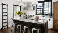 Warna hitam dan putih klasik menjadi latar belakang dapur ini. Trim jendela dan pintu yang dicat hitam kontras dengan dinding ubin yang putih menambah kesan modern. Meja dapur dari baja tahan karat dan bangku dari aluminium memainkan gaya modern dan industrial. Foto: WERNER STRAUBE via Better Homes & Gardens