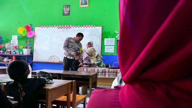 Seorang anak bernama Ilham Ramadhan (8) meminta polisi menemaninya saat pembagian rapor.