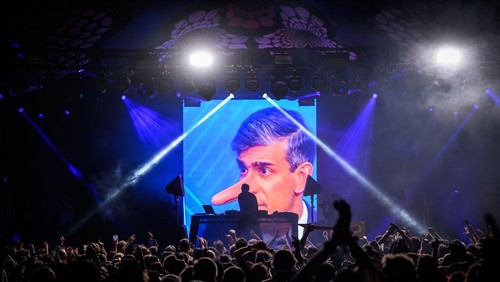 GLASTONBURY, ENGLAND - JUNE 30: Fatboy Slim is silhouetted against graphics as he performs on the Glade State in the early hours of day five of Glastonbury Festival 2024 at Worthy Farm, Pilton on June 30, 2024 in Glastonbury, England. Founded by Michael Eavis in 1970, Glastonbury Festival features around 3,000 performances across over 80 stages. Renowned for its vibrant atmosphere and iconic Pyramid Stage, the festival offers a diverse lineup of music and arts, embodying a spirit of community, creativity, and environmental consciousness. (Photo by Leon Neal/Getty Images)