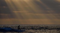 Seorang peselancar sendirian menangkap ombak saat matahari terbenam di balik awan di Pantai Cardiff, Encinitas, California, AS, 1 Juli 2024.