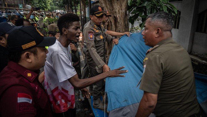 Momen Satpol PP Bongkar Tenda Pengungsi WNA di Depan Gedung UNCHR Petugas Satpol PP membongkar tenda pengungsi warga negara asing (WNA) saat penertiban di depan Kantor UNCHR, kawasan Kuningan, Jakarta, Selasa (2/7/2024). Pemerintah Provinsi DKI Jakarta menertibkan sebanyak 15 WNA yang mendirikan tenda untuk ditempatkan di rumah detensi imigrasi sesuai Undang-Undang Nomor 6 Tahun 2011 Pasal 75 tentang keimigrasian. ANTARA FOTO/Bayu Pratama S/foc.