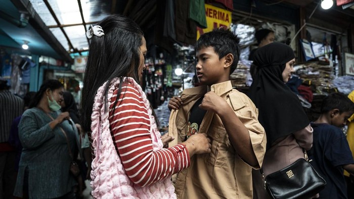 Pedagang (kiri) membantu seorang anak saat mencoba seragam sekolah di Pasar Jatinegara, Jakarta, Selasa (2/7/2024). Menurut pedagang menjelang tahun ajaran baru 2024/2025 yang akan dimulai pada Senin (8/7), penjualan seragam sekolah yang dijual mulai Rp75 ribu-Rp200 ribu itu mengalami peningkatan hingga lima kali lipat dibanding hari biasa. ANTARA FOTO/Aprillio Akbar/nym.