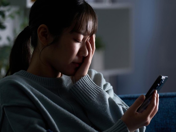 2149628216 A depressed woman looking at her smartphone