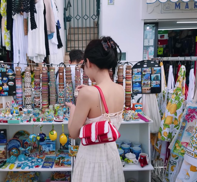 Sebelum pulang ke Korea Selatan, Jennie BLACKPINK cuci mata melihat barang-barang lucu yang dijual pedagang lokal. CEO ODD ATELIER memilih paduan long dress berwarna krem dari AND YOU seharga Rp 3,2 juta dan koleksi tas merah Jacquemus La Petit Bambimou bernilai Rp 16,7 juta. Foto: dok. YouTube jennierubyjane