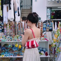 Sebelum pulang ke Korea Selatan, Jennie BLACKPINK cuci mata melihat barang-barang lucu yang dijual pedagang lokal. CEO ODD ATELIER memilih paduan long dress berwarna krem dari AND YOU seharga Rp 3,2 juta dan koleksi tas merah Jacquemus La Petit Bambimou bernilai Rp 16,7 juta. Foto: dok. YouTube jennierubyjane