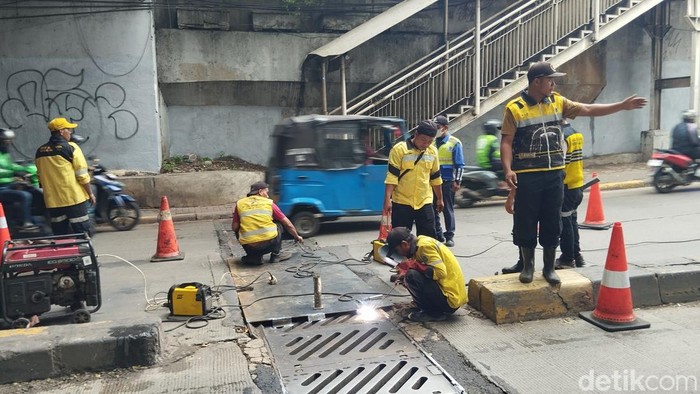 Petugas Bina Marga memperbaiki penutup gorong-gorong underpass Manggarai yang macet.