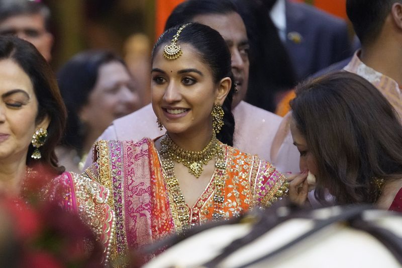 Radhika Merchant, fiancée of Anant Ambani, the son of Chairman of Reliance Industries Limited, Mukesh Ambani, centre, smiles during her pre-wedding ceremony at Antilia in Mumbai, India, Wednesday, July 3, 2024. (AP Photo/Rafiq Maqbool)
