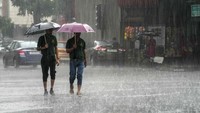 Pejalan kaki menerobos hujan menggunakan payung.