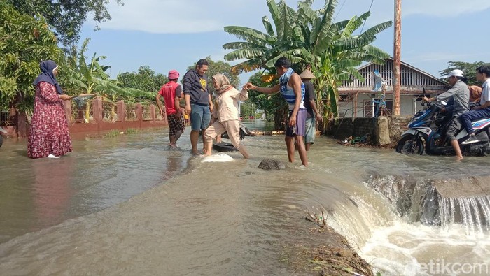 Potret warga bergotong royong membantu pengguna jalan akibat akses jalan utama tertutup baniir di Desa Tinumpuk, Kecamatan Juntinyuat, Kabupaten Indramayu, Senin (8/7/2024).