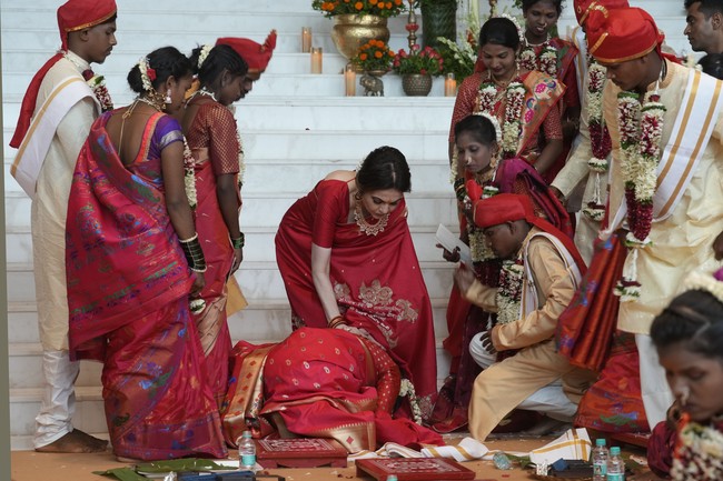 Salah satu peserta nikah massal berlutut di hadapan Nita Ambani sebagai bentuk ungkapan terima kasih. Nita juga berbalut saree merah, tapi gayanya maksimal dipadu perhiasan mewah. (Foto: AP Photo/Rafiq Maqbool)