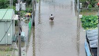 Seorang wanita membawa barangnya berjalan di tengah banjir.  