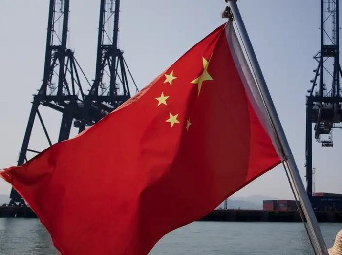 Sebuah bendera China yang sedang berkibar di depan mesin pengangkut kargo di pelabuhan di China (Foto: Daniel Berehulak/Getty Images)