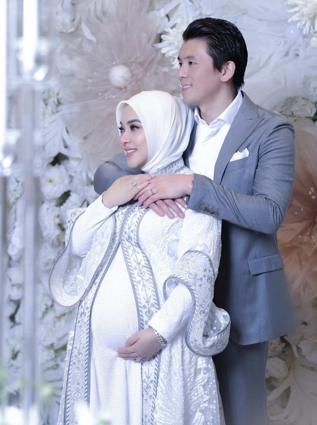 Ini momen Syahrini merayakan tujuh bulan kehamilan bersama sang suami. Pilihan gamis putih dilengkapi long outerwear yang kaya akan detail mungkin bisa menginspirasi para bumil. Foto: Instagram @princessyahrini