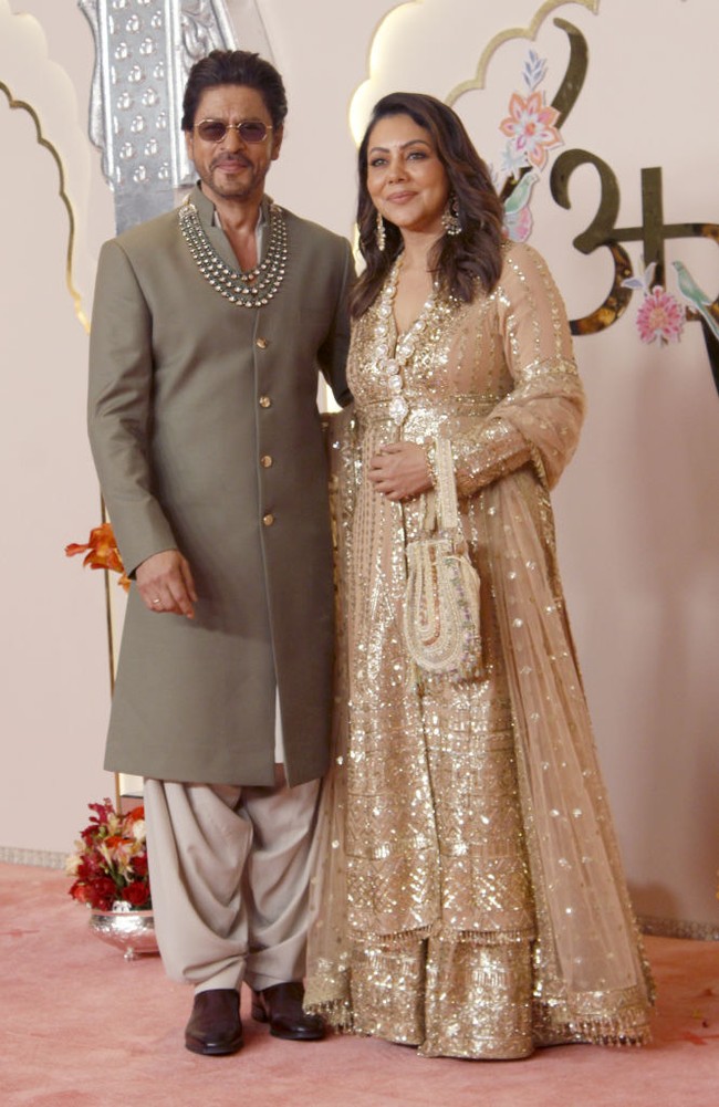 Aktor Shah Rukh Khan menggandeng sang istri, Gauri Khan, saat berpose untuk fotografer sebelum memasuki venue acara. Shahrukh memakai jas panjang warna hijau tua. Foto: Getty Images