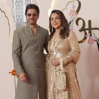 Aktor Shah Rukh Khan menggandeng sang istri, Gauri Khan, saat berpose untuk fotografer sebelum memasuki venue acara. Shahrukh memakai jas panjang warna hijau tua. Foto: Getty Images