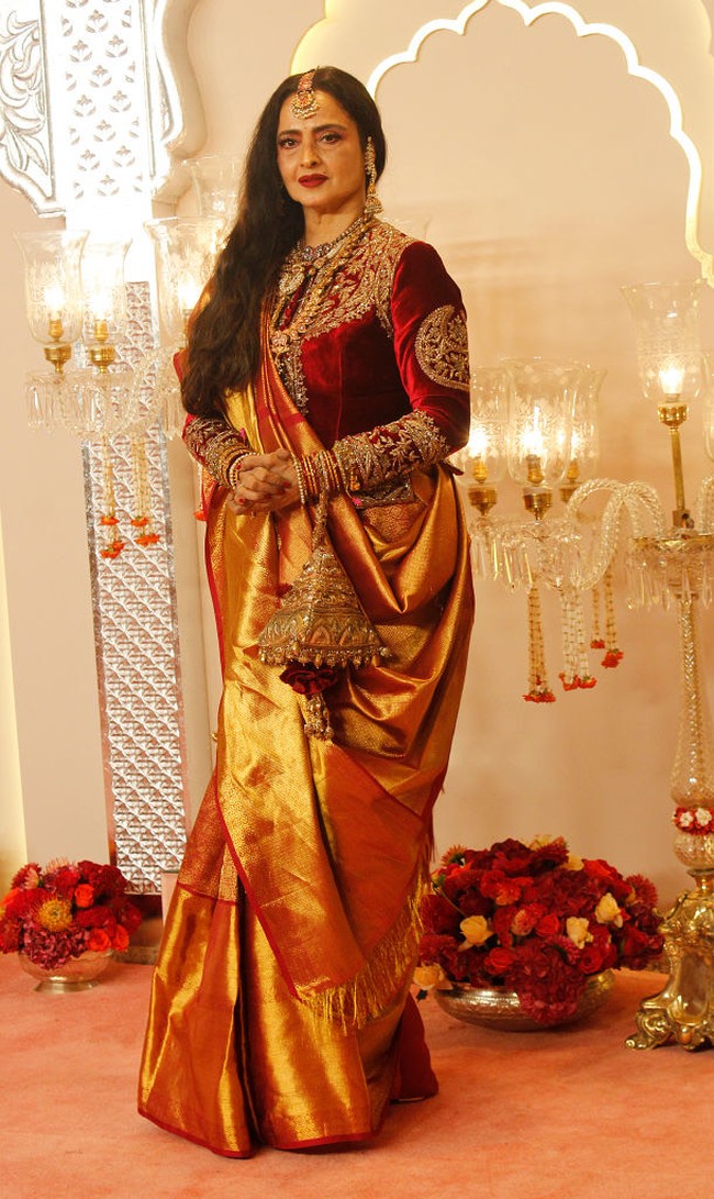 Aktris kawakan Rekha tampil anggun dengan busana beludru warna merah yang dipadukan kain saree warna oranye metalik. Foto: Getty Images