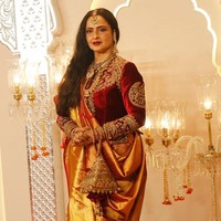 Aktris kawakan Rekha tampil anggun dengan busana beludru warna merah yang dipadukan kain saree warna oranye metalik. Foto: Getty Images