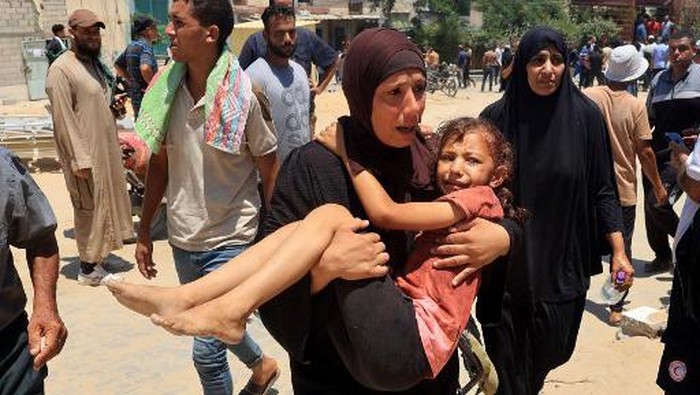 A Palestinian woman carries an injured child to the Nasser hospital in Khan Yunis on July 13, 2024, one of the health establishments to which casualties were rushed after an Israeli strike killed at least 71 people and injured many others at the Al-Mawasi camp for the war displaced in the south of the Palestinian territory, according to the Hamas-run health ministry. The Israeli military said the strike on the tent city with tens of thousands of people had aimed at two Hamas officials. (Photo by Eyad BABA / AFP)