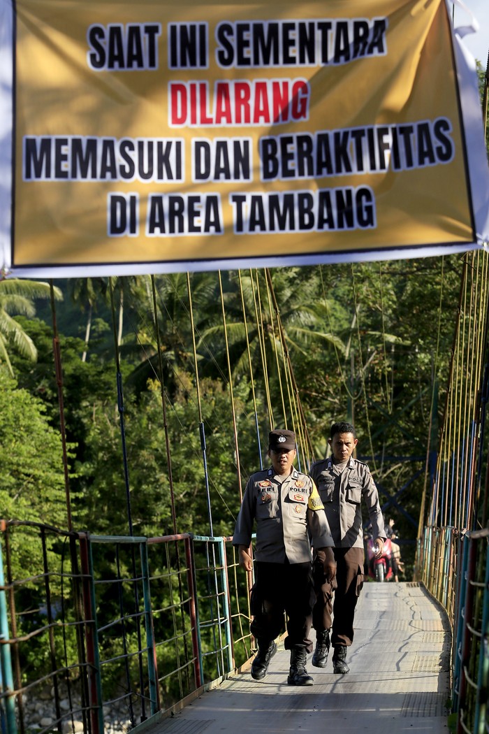 Anggota Polsek Suwawa berbincang dengan pengemudi ojek motor di jembatan gantung yang menjadi pintu masuk menuju tambang rakyat di Desa Tulabolo, Suwawa Timur, Kabupaten Bone Bolango, Gorontalo, Minggu (14/7/2024). Forum Komunikasi Pimpinan Daerah (Forkopimda) Kabupaten Bone Bolango menutup sementara aktivitas tambang emas rakyat pascabencana tanah longsor yang mengakibatkan 27 orang meninggal dunia dan 15 orang hilang. ANTARA FOTO/Adiwinata Solihin/rwa.