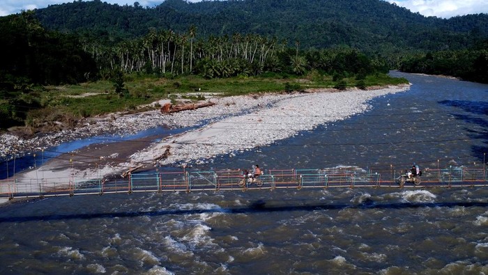 Anggota Polsek Suwawa berbincang dengan pengemudi ojek motor di jembatan gantung yang menjadi pintu masuk menuju tambang rakyat di Desa Tulabolo, Suwawa Timur, Kabupaten Bone Bolango, Gorontalo, Minggu (14/7/2024). Forum Komunikasi Pimpinan Daerah (Forkopimda) Kabupaten Bone Bolango menutup sementara aktivitas tambang emas rakyat pascabencana tanah longsor yang mengakibatkan 27 orang meninggal dunia dan 15 orang hilang. ANTARA FOTO/Adiwinata Solihin/rwa.