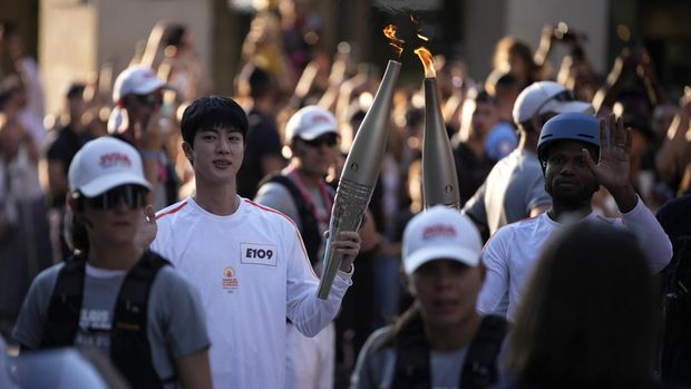 Jin, anggota tertua supergrup K-pop BTS, membawa obor Olimpiade, Minggu, 14 Juli 2024 di Paris. (AP Photo/Louise Delmotte)