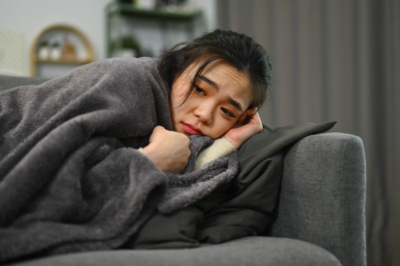 Sick mature woman wrapped blanket lying on couch, suffering high fever or seasonal flu. Health care concept.