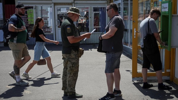 Perang Masih Bergejolak, Ukraina Gencarkan Rekrutmen Wajib Militer A recruiters officer with the call sign 'Fantomas' speaks with a man on a street as he checks papers of men and hands out military summonses, amid Russia's attack on Ukraine, in Kyiv, Ukraine July 3, 2024. REUTERS/Gleb Garanich