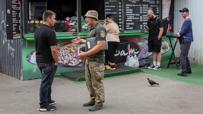 Perang Masih Bergejolak, Ukraina Gencarkan Rekrutmen Wajib Militer A recruiters officer with the call sign 'Fantomas' speaks with a man on a street as he checks papers of men and hands out military summonses, amid Russia's attack on Ukraine, in Kyiv, Ukraine July 3, 2024. REUTERS/Gleb Garanich