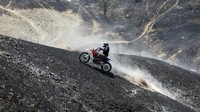 Seorang relawan mengendarai sepeda motor melintas di kawasan hutan yang hangus terbakar.