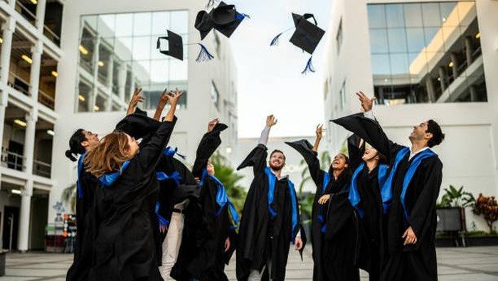 Young graduates throwing their mortarboard in the air while celebrating on graduation