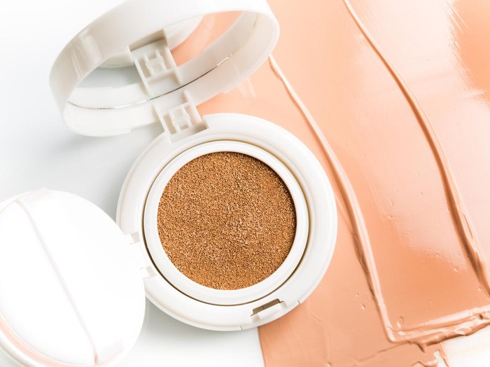 Foundation cushion with sponge and puff on half of the surface of a tonal base, smeared on a white background