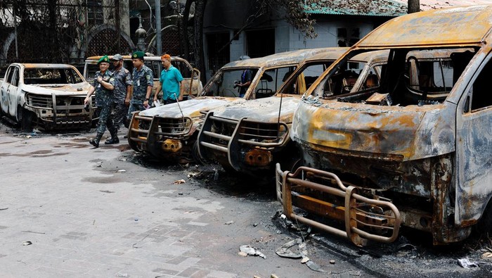 Security personnel walk past damaged vehicles of a government owned organization, that were set afire by a mob during clashes after violence erupted following protests by students against government job quotas, in Dhaka, Bangladesh, July 22, 2024. REUTERS/Mohammad Ponir Hossain