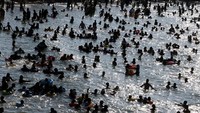 Para wisatawan mengajak keluarganya untuk berenang ke pantai di tengah panasnya cuaca.