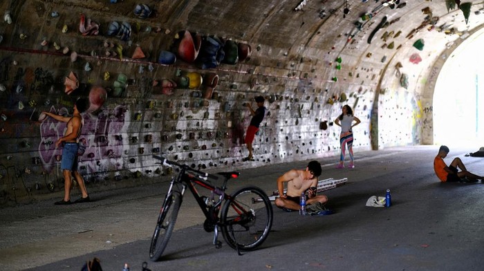 Unik, Bekas Terowongan 'Disulap' Jadi Arena Panjat Dinding David Sanchez, 18, climbs helped by Carlos Gallardo, 65, at the wall of the Foixarda tunnel, which was transformed from a former road tunnel into an urban, free-to-use climbing gym open at all times, equipped with thousands of holds, in Barcelona, Spain June 26, 2024. REUTERS/Nacho Doce