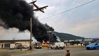 Sebuah pesawat melintas di atas kebakaran yang mulai merembet mendekati depo bus di kawasan Cariboo, British Columbia, Kanada, Minggu (21/7/2024) waktu setempat.