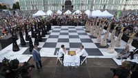 Pemenang Kejuaraan Catur Dunia FIDE 1999 Alexander Khalifman, kanan, dan pemenang Kejuaraan Catur Perorangan Eropa 2017 Maxim Matlakov memainkan permainan catur sementara para aktor berpakaian bidak catur memperagakan permainan ini di papan catur besar selama perayaan Hari Catur Internasional di Lapangan Dvortsovaya (Istana) Petersburg, Rusia, Sabtu (20/7).