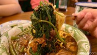 Mie kangkung berisi topping daging ayam berukuran besar, lembaran kangkung, taburan bawang goreng, dan irisan jeruk limau.