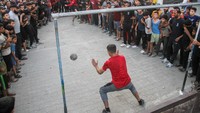 Berdiri di luar tenda dan balkon mereka, keluarga-keluarga pengungsi dan anak-anak mereka menyaksikan dan bersorak saat tim berkompetisi.  