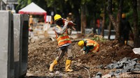 Pekerja tampak sibuk dengan pekerjaan masing-masing, ada yang menggali dan mengangkut material bangunan.  