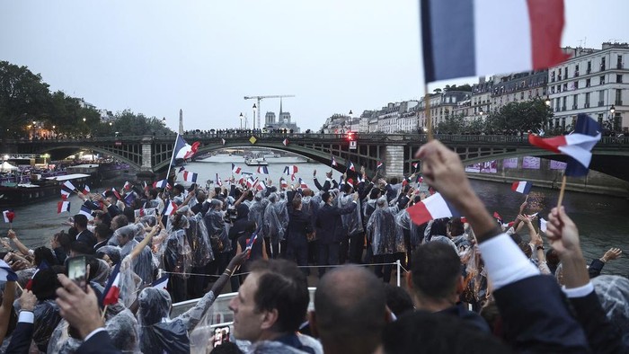 French athletes wave flags as they sail in a boat on the river Seine during the opening ceremony for the 2024 Summer Olympics in Paris, France, Friday, July 26, 2024. (Franck Fife/Pool Photo via AP)