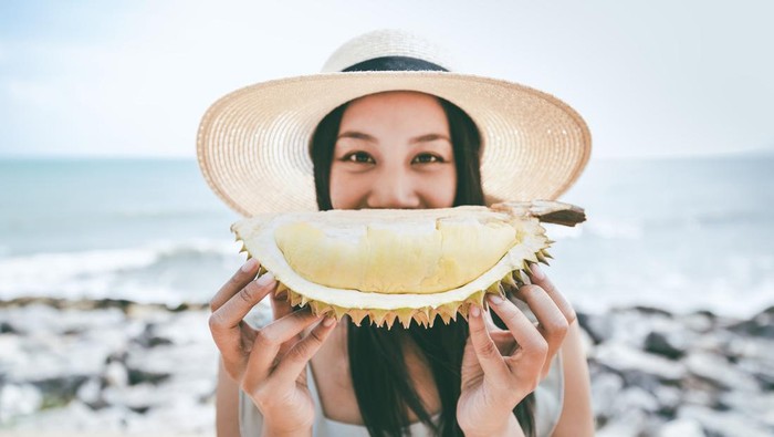 Happy asian woman Holding durian fruit on tropical beach in Thailand
