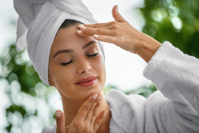 Young woman massaging face with her eyes closed. Shes in the bathrobe and her hair is wrapped in the towel.