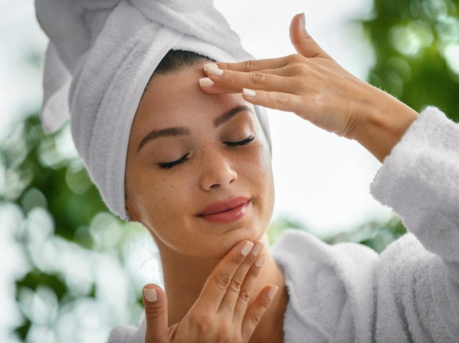 Young woman massaging face with her eyes closed. Shes in the bathrobe and her hair is wrapped in the towel.