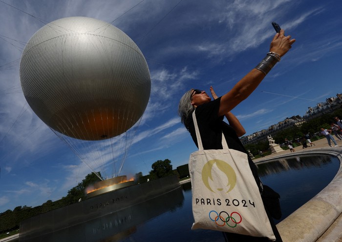 Paris 2024 Olympics - Paris, France - July 28, 2024 A person takes a selfie by the Olympic cauldron during the Olympics REUTERS/Kai Pfaffenbach