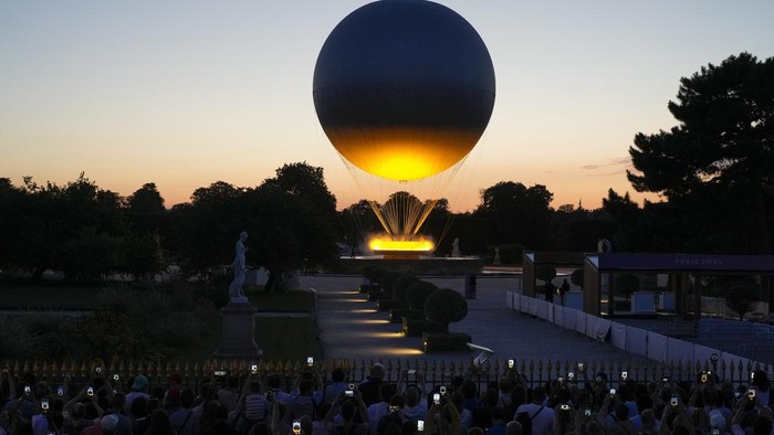 Menikmati Senja Paris yang Berhias Kaldron Olimpiade 2024 A crowd takes photos at the Tuileries Garden as the cauldron rises at sunset during the 2024 Summer Olympics, Sunday, July 28, 2024, in Paris, France. (AP Photo/Natacha Pisarenko)