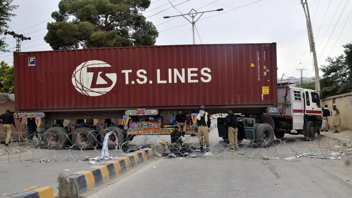 Police officers guard a road blocked by a shipping container and truck, Monday, July 29, 2024,  in Quetta, Pakistan. In Baluchistan province in Pakistan’s southwest, meanwhile, thousands protested against police violence, an internet shutdown and highway closures, community leaders said Monday. (AP Photo/Arshad Butt)