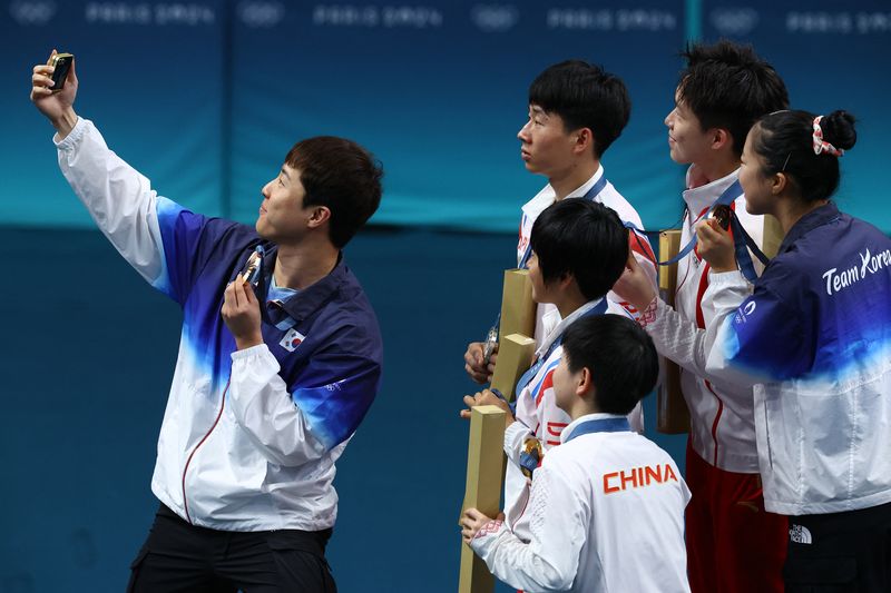 Paris 2024 Olympics - Table Tennis - Mixed Doubles Victory Ceremony - South Paris Arena 4, Paris, France - July 30, 2024. Bronze medallist Jonghoon Lim of South Korea takes selfie with Yubin Shin of South Korea and gold medallists Chuqin Wang of China and Yingsha Sun of China with silver medallists Jong Sik Ri of North Korea and Kum Yong Kim of North Korea on the podium with their medals after winning. REUTERS/Stephanie Lecocq