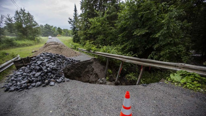 Trees sit across a roadway destroyed by flash floods in Lyndonville, Vt., Wednesday, July 31, 2024. Parts of the state hit by flooding Monday night and Tuesday are bracing again as a new round of severe thunderstorms moves through the region. (AP Photo/Nick Perry)